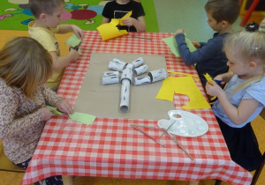 Pięcioro dzieci siedzi przy stoliku i wycina po śladzie listki z papieru.